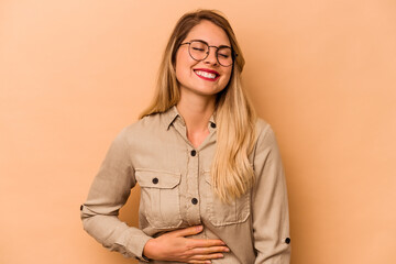 Young caucasian woman isolated on beige background touches tummy, smiles gently, eating and satisfaction concept.