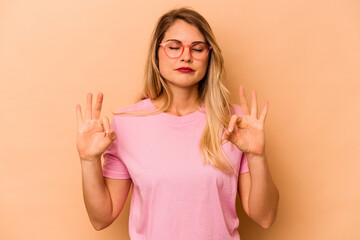 Young caucasian woman isolated on beige background relaxes after hard working day, she is performing yoga.