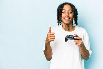 Young African American man playing with a video game controller isolated on blue background smiling...