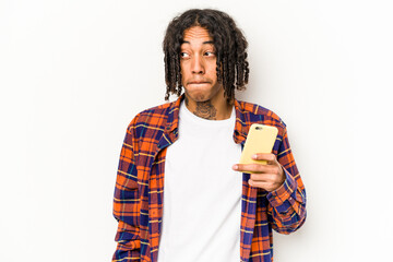 Young African American man holding mobile phone isolated on white background confused, feels...