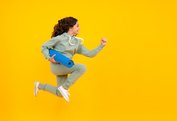 Fototapeta na wymiar Run and jump. Sportswear advertising concept. Teenager child girl in tracksuits jogging suit posing in the studio hold fitness mat.
