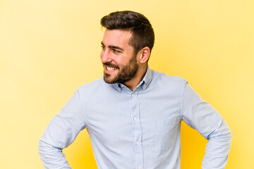 Young caucasian man isolated on yellow background laughs happily and has fun keeping hands on stomach.