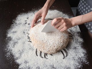 Baker's hand cuts raw yeast-free dough on a dark background with a plastic knife.