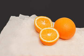 Two oranges, one of which has been cut. The fruits lie on white paper with a black background on the back. - 510664276
