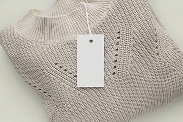 White blank rectangle price tag hanging on knitted sweater, label mockup for care instruction, logo...