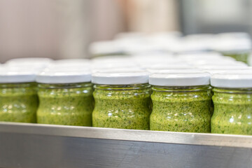 Pesto sauce Industrial process. High quality sauce production. Green pesto sauce in jars on a food factory table. Italian basil taste in Pesto sauce