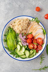 Healthy bowl lunch with grilled chicken, quinoa, avocado, tomatoes, cucumbers and fresh arugula on gray background. Top view. Selective focus.