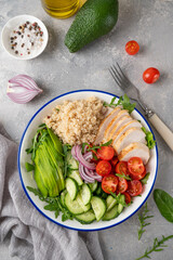 Healthy bowl lunch with grilled chicken, quinoa, avocado, tomatoes, cucumbers and fresh arugula on gray background. Top view. Selective focus.