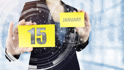 January 15th. Day 15 of month, Calendar date. Business woman hand hold yellow sheet with calendar date on blurred office background. Winter month, day of the year concept.