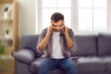 Man suddenly feels dizzy and takes a seat on the sofa. Young guy feeling pain and spinning...