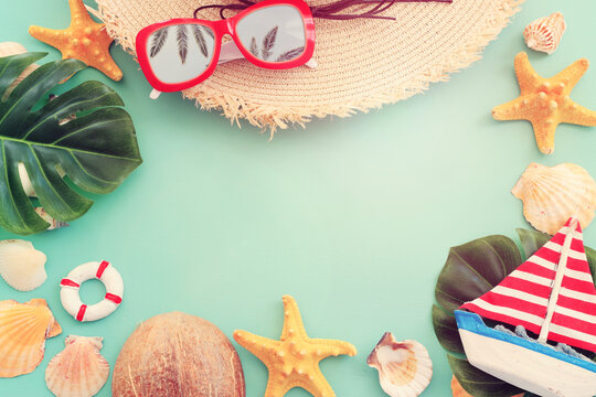 nautical concept with tropical leaf, beach hat, seashells and starfish over mint blue wooden background