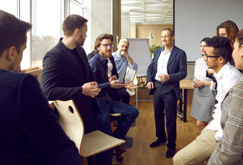 Various business colleagues communicate and joke in casual conversation at briefing in loft...