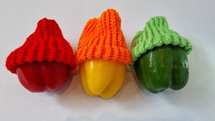 Raw, whole large red, orange and green peppers with the same colour loom knitted woollen hats lay...