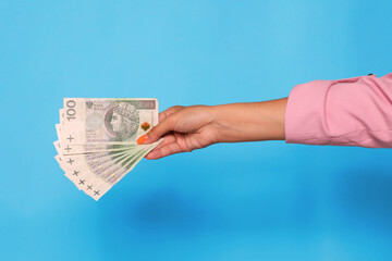 Hand holding polish zloty currency over blue background