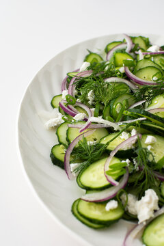 Light summer salad of cucumbers, onions and feta cheese in an oval white dish, close-up