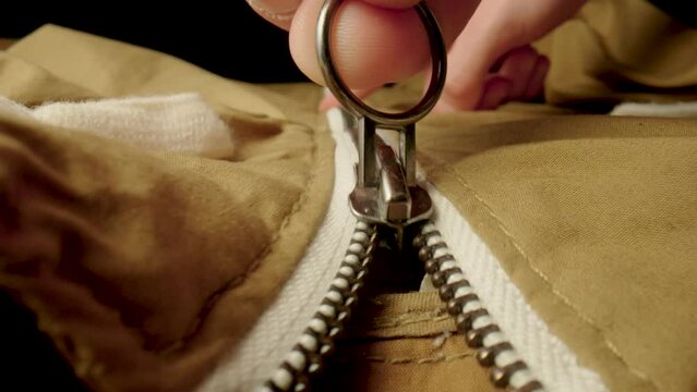 A man fastens a metal zipper on a beige jacket in macro. Extreme close up zipper with hand fastens clothing, while camera following the man hand. Fashion, textile and clothing industry concept.