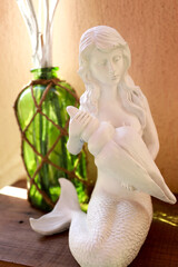 A white statue of a mermaid with a clam and a green glass vase with strings.