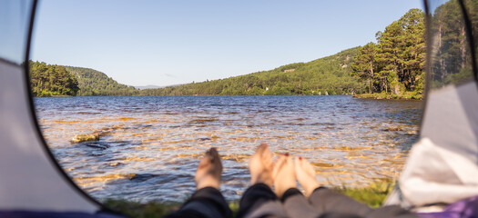 Photo of feet inside of a tent which is located in front of a lake during a summer morning in Scotland