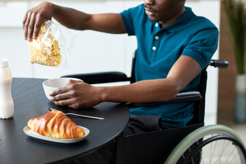 Close up of black adult man with disability eating cereal for breakfast in elegant home kitchen, copy space
