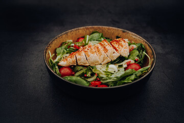 Colorful mixed salad of cucumber, cherry tomatoes and arugula with fried chicken breast in a bowl