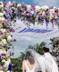 Jewish couple at a marriage ceremony under a chuppa canopy. Canopy is inscribed with words from ...