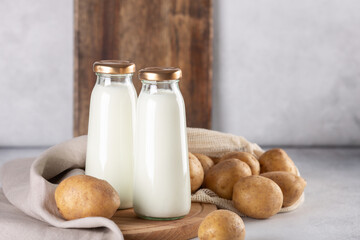 Bottles with vegan plant based milk. Dairy-free drink and potato tubers on gray table