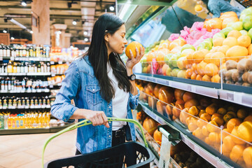 Young woman in supermarket near shelf with fruits chooses oranges