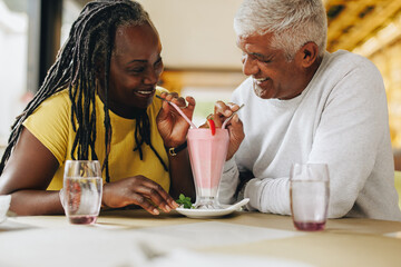 Happy mature couple sharing a delicious milkshake in a cafe