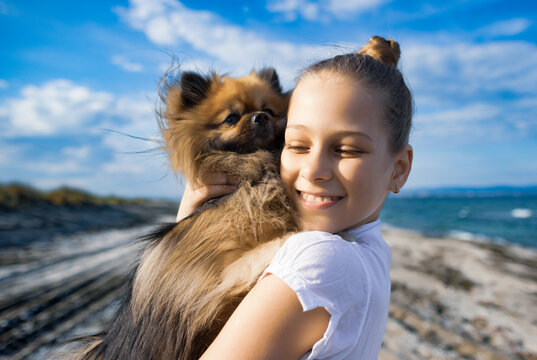 Girl with blond hair with smile hugs pomeranian dog with golden hair on seashore near Black Sea