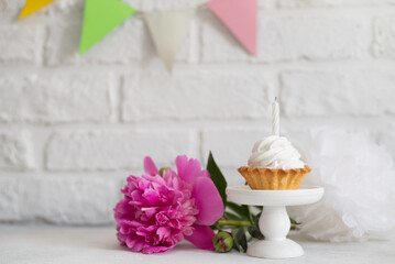 Fototapeta na wymiar Cake with a candle on a cake stand in a background of a white brick wall, pink flowers and colorful flags.