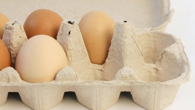 Close up of ten chicken eggs in a cardboard tray on the table. Female hands fold eggs in a tray.
