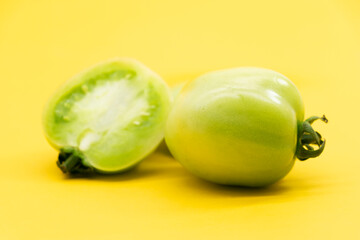 Whole and halved green unripe tomatoes isolated on yellow background