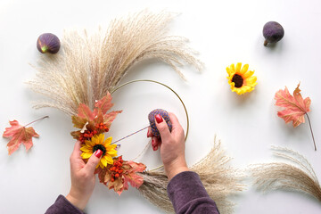Hands making dried floral wreath from dry pampas grass and Autumn leaves. Hands in sweater with...