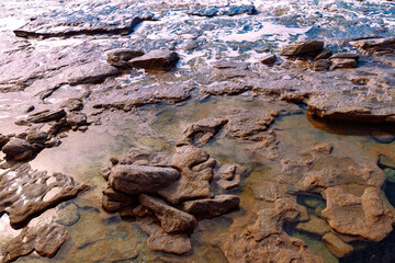 Beautiful landscape of rocky coast, rolling sea waves and sun reflection in water. Selective focus.