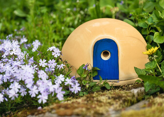 Cute ceramic house with attractive blue door for nesting bumble bees on a spring garden around...