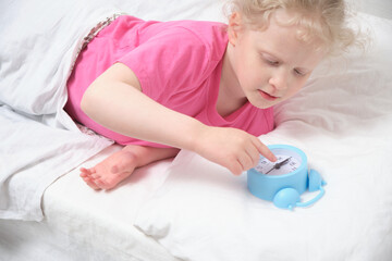 Obraz na płótnie Canvas child and alarm clock, girl lying on bed checks alarm clock, healthy child sleep concept