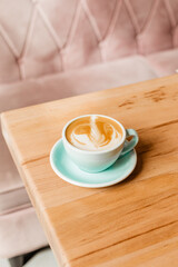 Beautifully made cappuccino with delicious foam on a wooden table. Coffee with milk and art latte in a blue ceramic mug. Stylish coffee serving in the restaurant. Creative concept for advertising