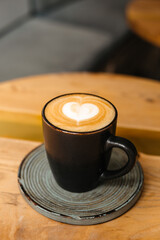 Fragrant cappuccino with beautiful foam and latteart in a black cup on a ceramic stand. Beautiful and stylish coffee serving