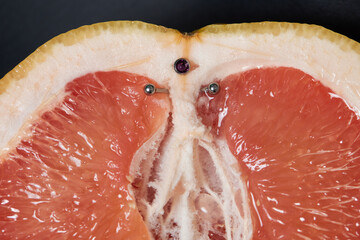 Half of grapefruit with vertical barbell piercing on a background.