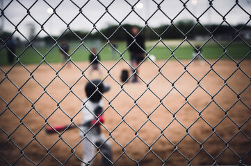 Selective focus on chain link fence with a youth baseball game defocused and blurred in the...