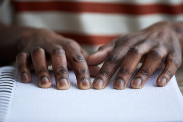 Macro shot of blind African American man reading book in braille, accessible information concept, copy space