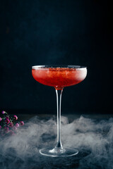 Strawberry daiquiri cocktail in a beautiful glass with crushed ice and smoke on a dark background. Tropical alcoholic drink with rum