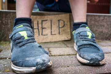 Kind in kaputten Schuhen und einem Schild mit dem Wort Hilfe in englischer Sprache
