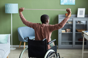 Back view of adult African American man with disability exercising at home using elastics