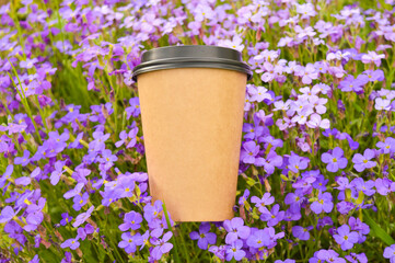 A mock-up of a paper cup for coffee or tea against a background aubrietta's purple flowers