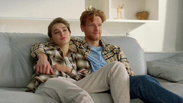 Sleepy couple watching tv together. Ginger man zapping channels in living room