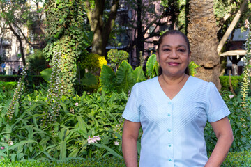 Mature Mexican woman looking at camera, smiling, standing in front of a garden. Latin woman looking at camera smiling. cheerful attitude.