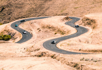 Cars driving on a winding road with yellow grass around