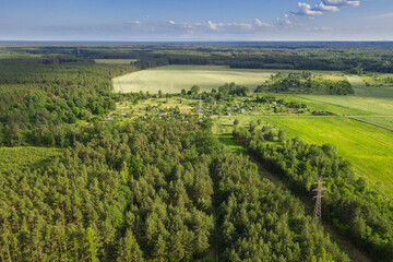 Fototapeta na wymiar Pola i łąki wiosną widziane z dużej wysokości. Zdjęcie z drona. Rozległy, płaski teren pokryty zielonymi polami uprawnymi i łąkami. Widać polną drogę, kępy drzew, oraz na obrzeżach iglasty las. Widok
