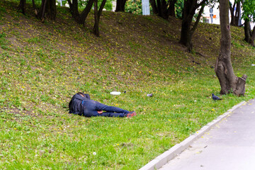 A drunk man in dirty clothes sleeps in the grass near the sidewalk